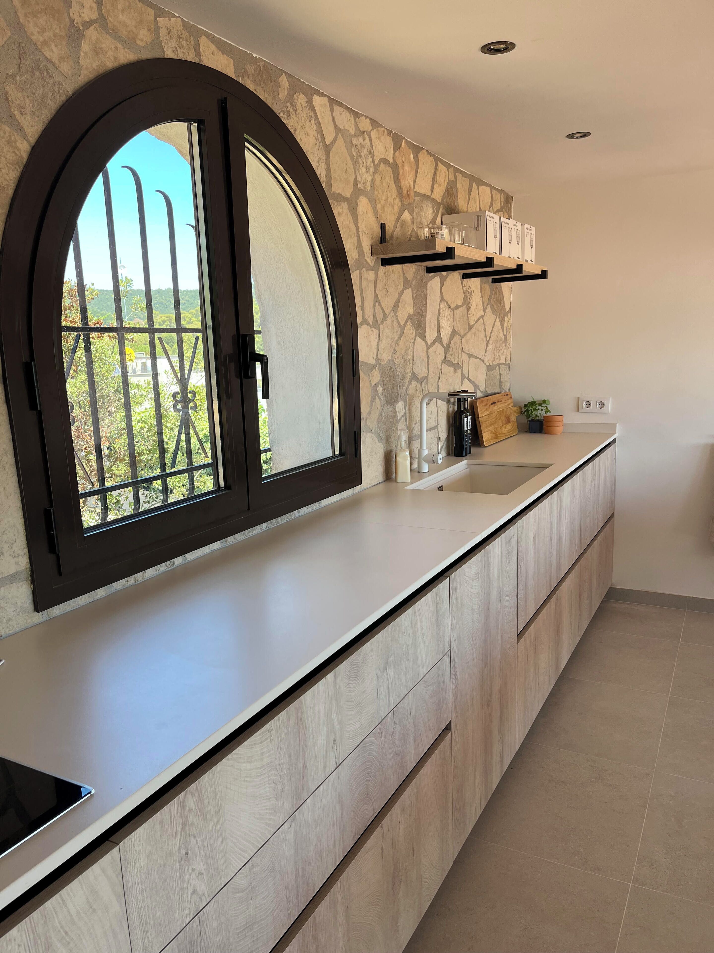 A modern kitchen with a stone backsplash, a large arched window, and built-in wooden cabinets.