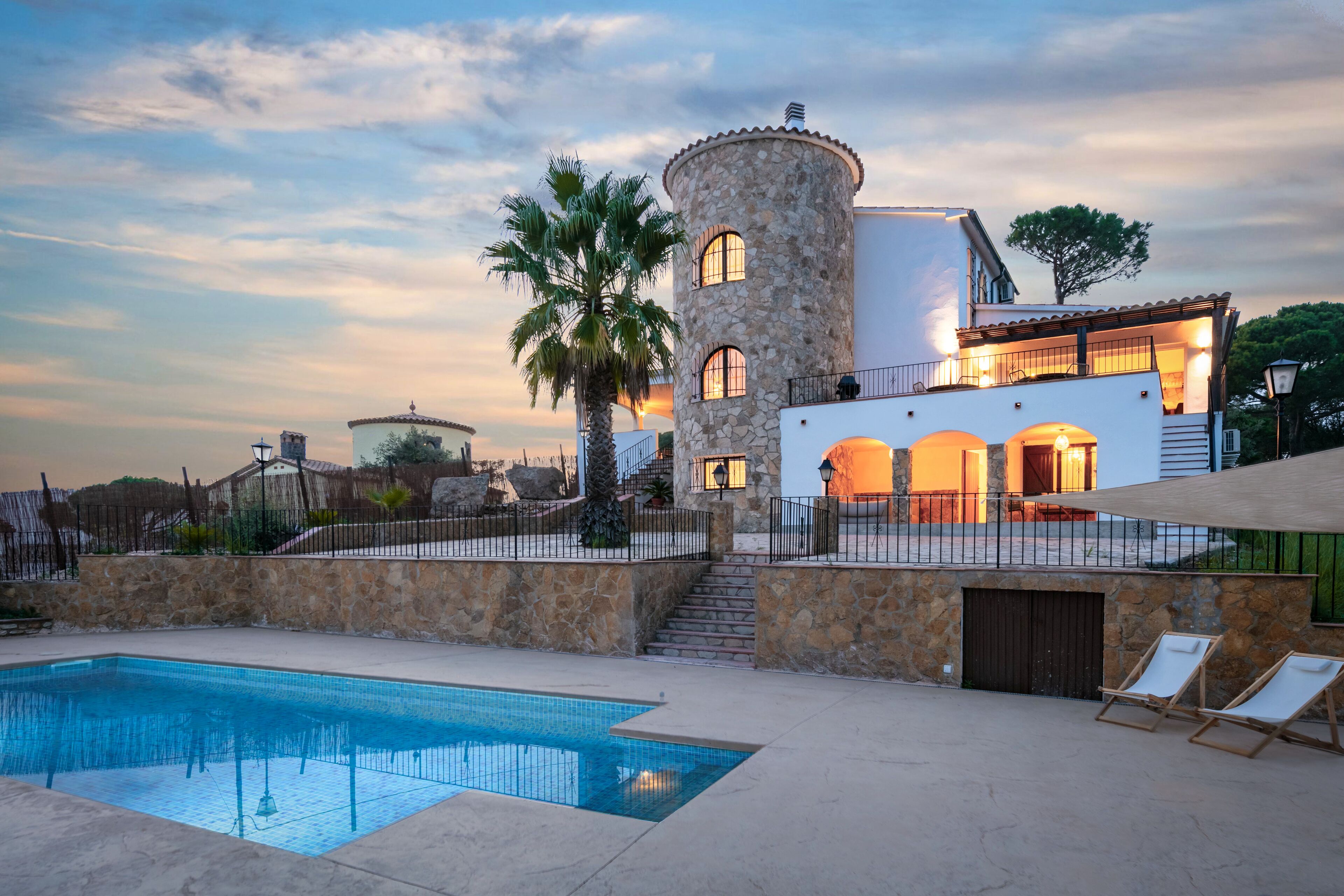 Una villa lujosa con piscina, torre de piedra y varios balcones.