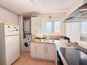 A compact kitchen with a built-in washing machine, a sink, and a stove. - Piso Grande y Reformado Para 4 Personas (Palamós)