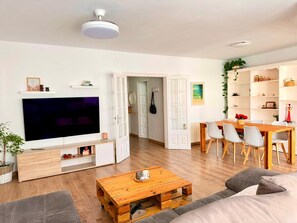 En moderne stue med et fladskærms-tv, et træsofabord, en sofa og et spiseområde med stole.