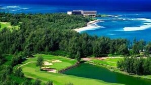 Vista aérea de un campo de golf con un extenso cuerpo de agua, un bosque denso y un edificio al fondo.