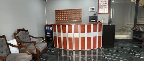 Un área de recepción con suelo de mármol, mostrador de recepción y dos sillones tapizados.