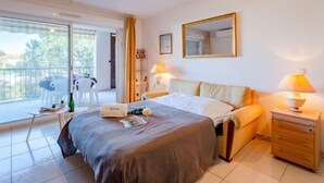 A hotel room with a bed, bedside table, lamp, and a view of the outside balcony. - Le Grand Parc by Interhome (Saint Aygulf)