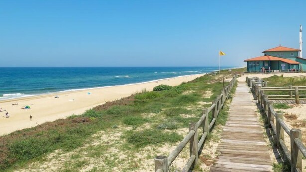 Een strand met een houten looppad dat naar een gebouw met een rood dak leidt.