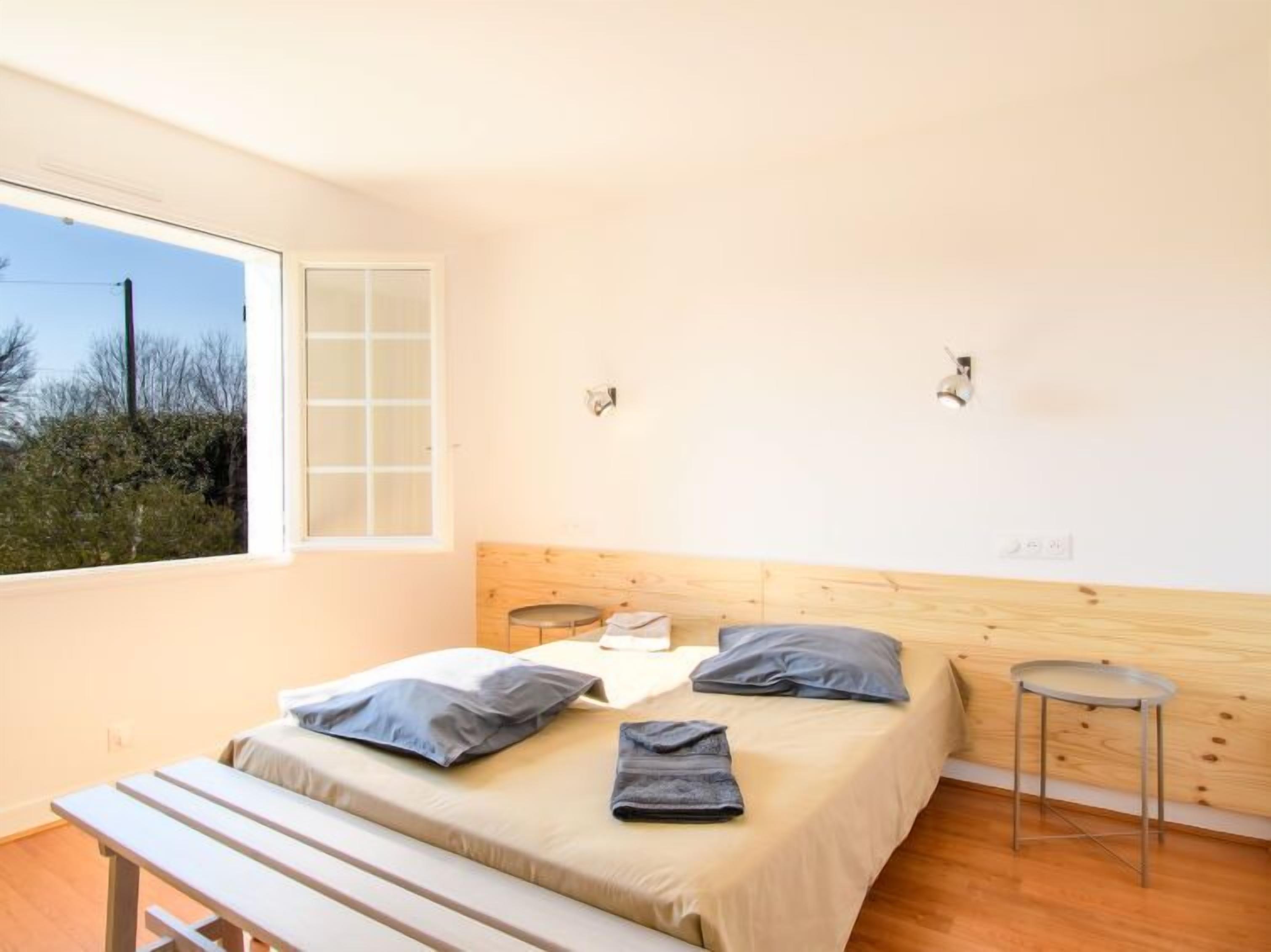 A bedroom with a bed, a bench, a small table, and a window.