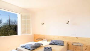 Een slaapkamer met een bed, een bankje, een kleine tafel en een raam.