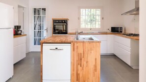 Een moderne keuken met witte kasten, een houten aanrechtblad, een ingebouwde oven, een magnetron en een raam dat voor natuurlijk licht zorgt.
