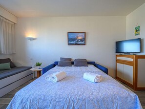 A bedroom with a bed, a TV, a painting, and a sofa.