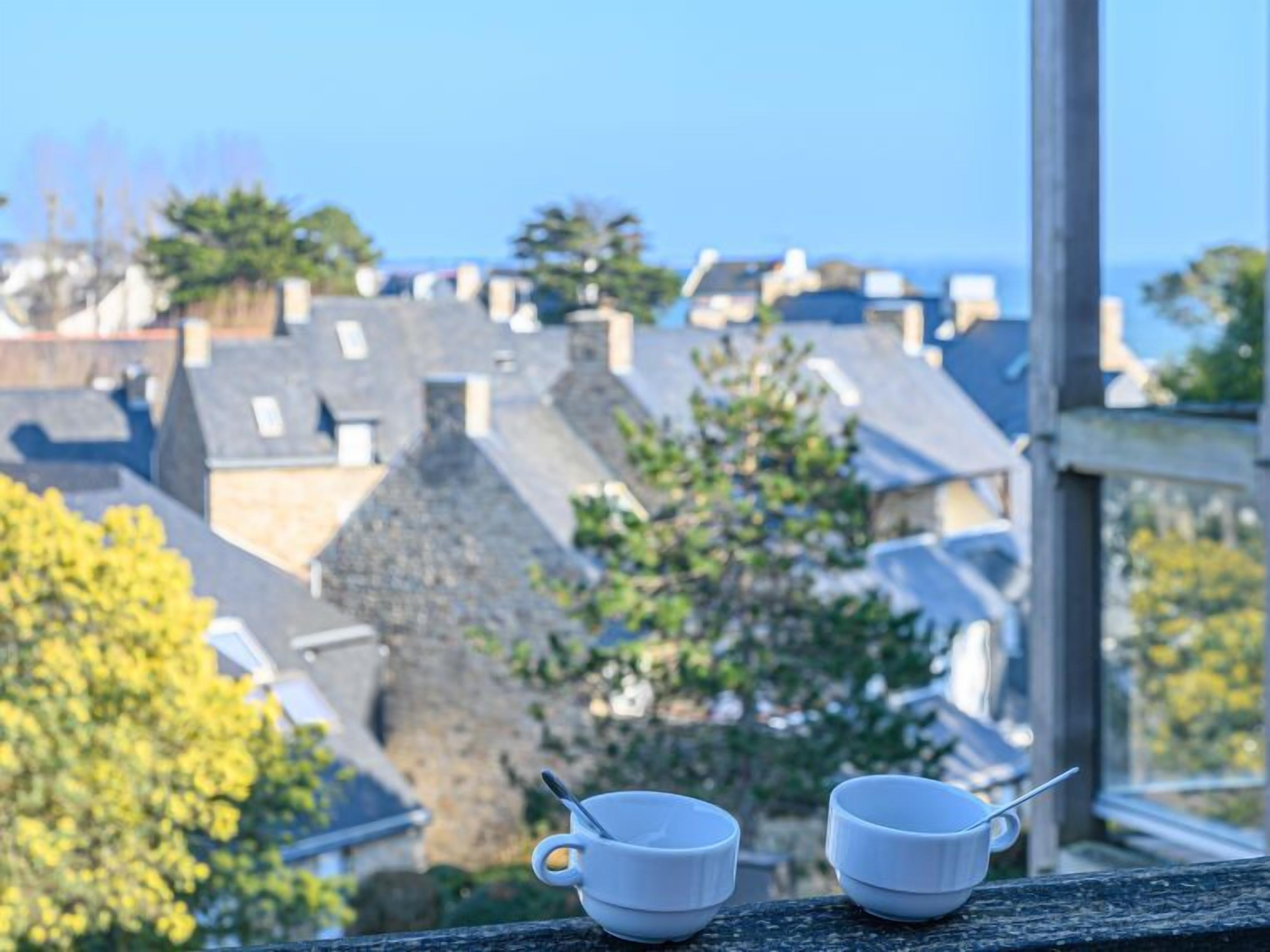 Two white cups on a balcony with a view of a town and trees.