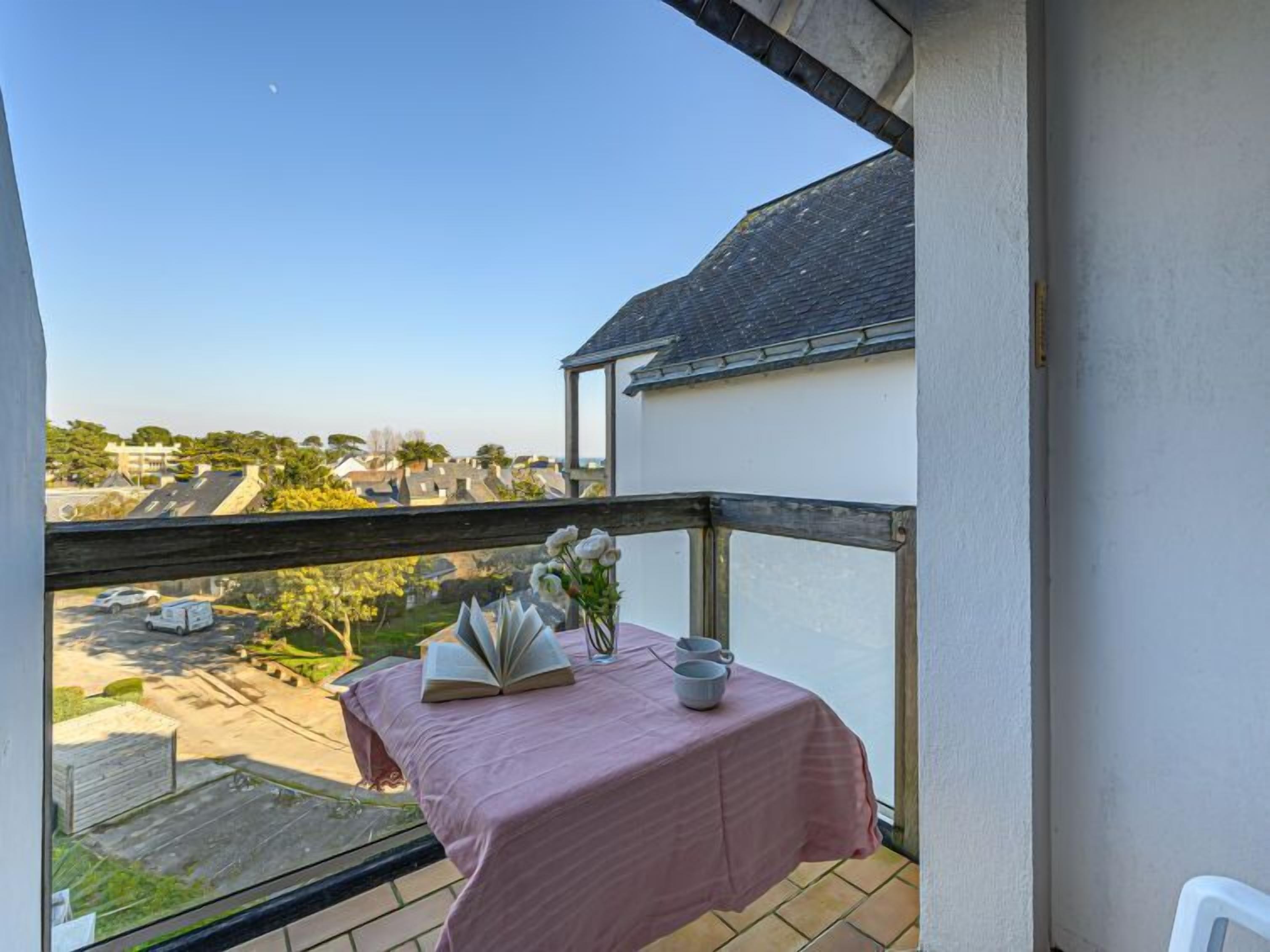 A balcony with a pink tablecloth, a book, and a vase with flowers.