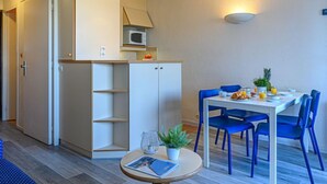 Un ambiente compatto con angolo cottura, un'area pranzo con sedie blu e un tavolino con una pianta e una rivista.