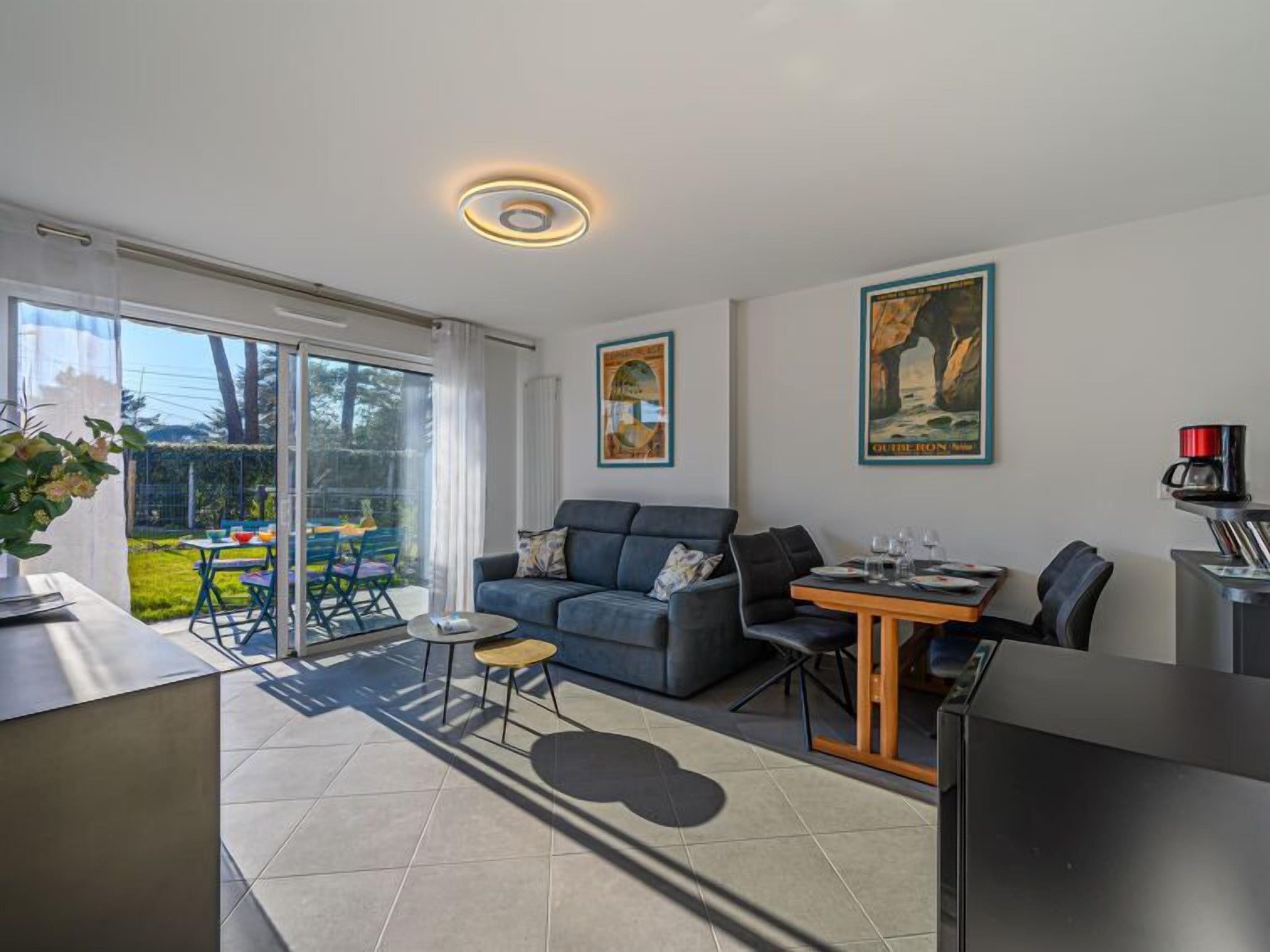 Un salon moderne comprenant un canapé, une table à manger et une machine à café. Une porte-fenêtre coulissante donne accès à un balcon aménagé avec du mobilier d’extérieur.