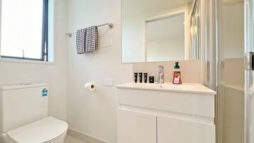 Une salle de bain comprenant des toilettes, un lavabo avec des articles de toilette, un miroir et une fenêtre.
