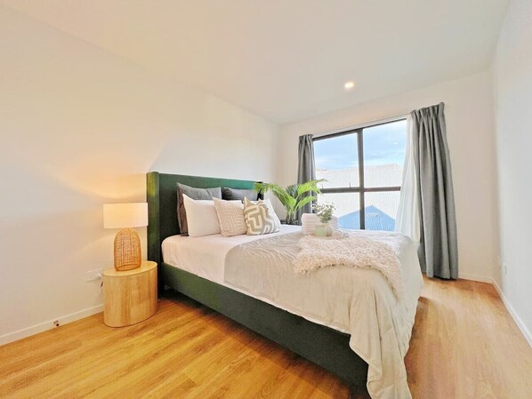 A modern bedroom with a bed, bedside table, lamp, and a window with curtains.
