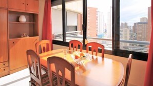 Un comedor con una mesa redonda, cuatro sillas y vistas a edificios altos a través de amplios ventanales.