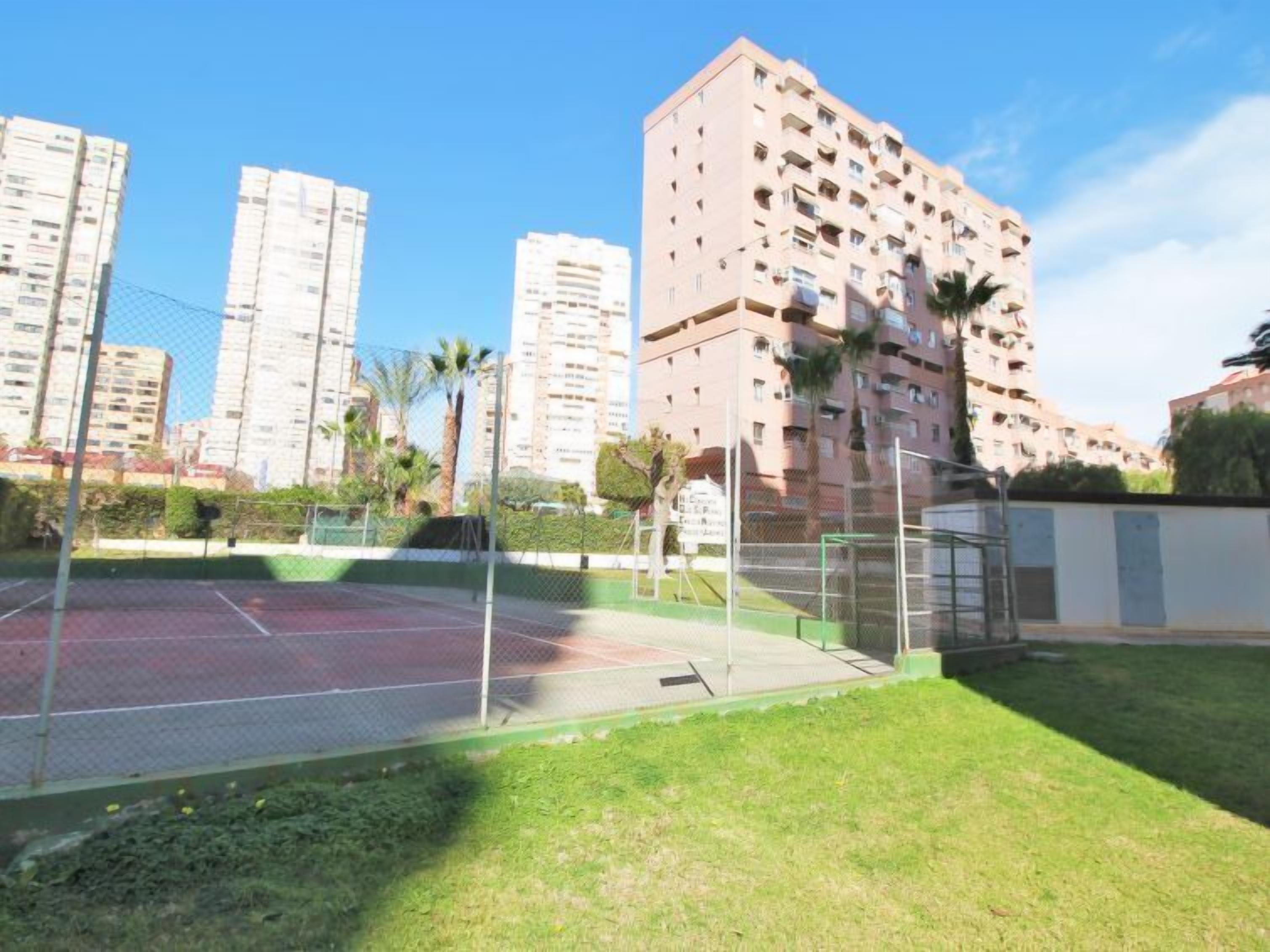 Een woongebied met hoge gebouwen, een tennisbaan en een gazon.