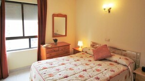 Un dormitorio con cama, cómoda, mesita de noche, lámpara, espejo y ventana con cortinas.