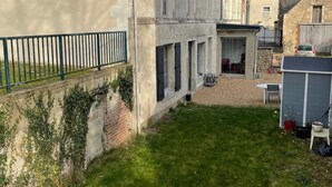 A courtyard with a grassy area, a brick wall with ivy, a metal fence, and a stone building with a car parked nearby. - Riverside Retreat: Cozy B&B with Bercé Forest Nearby, Ideal for Fishing & Hiking (Vaas)