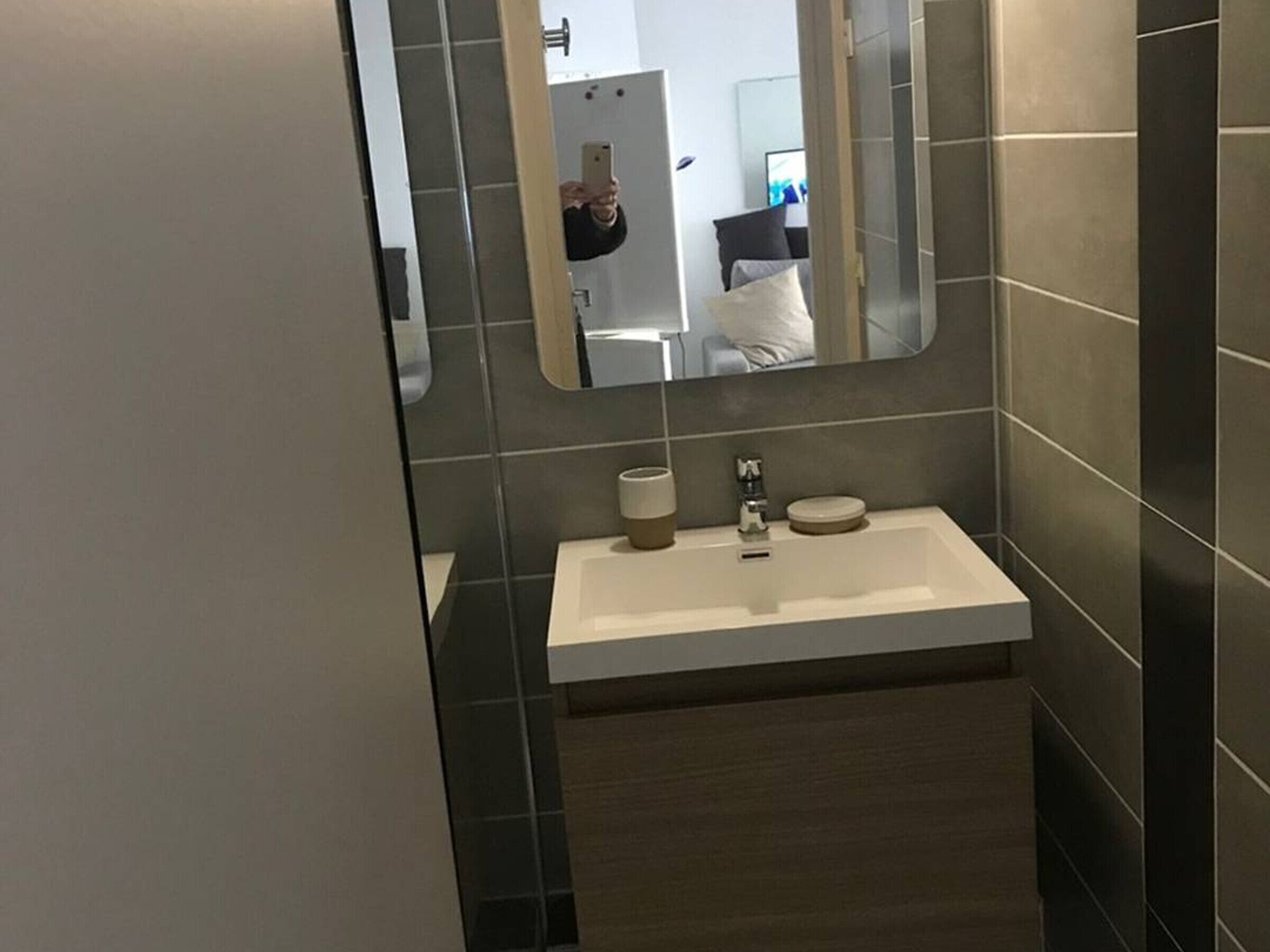 Une salle de bain moderne avec un lavabo blanc, des carreaux foncés et un miroir.