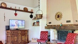 Een woonkamer met een televisie, houten meubels, rode stoelen, een open haard en decoratieve objecten aan de wand.