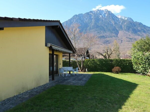 A yellow building with a patio area, a mountain in the background, and a well-maintained lawn. - Dorenavant by Interhome (Le Bouveret)