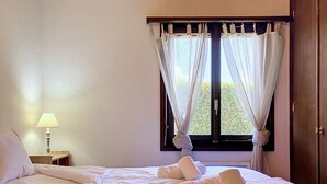 Een hotelkamer met een bed, een nachtkastje met een lamp en een raam met gordijnen.