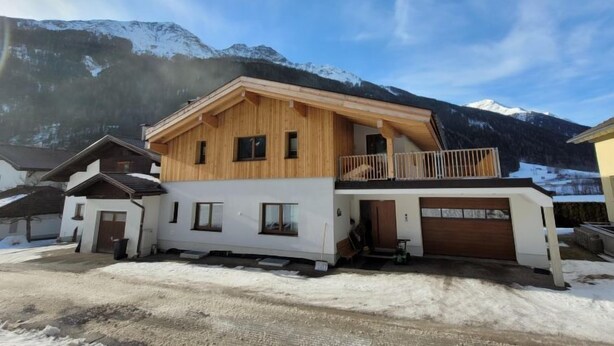 A two-story wooden house with a balcony, garage, and a view of snow-covered mountains. - Freiheit-La by Interhome (Pettneu am Arlberg)