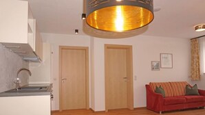 A modern room with a bed, a red sofa, a kitchen area, and two wooden doors. - Freiheit-La by Interhome (Pettneu am Arlberg)