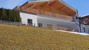 A modern two-story building with a wooden balcony and a stone retaining wall. - Freiheit-La by Interhome (Pettneu am Arlberg)