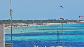 Una playa con aguas azules cristalinas, una orilla arenosa y un paracaídas en el cielo.