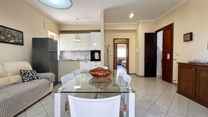 Una cocina moderna con armarios blancos, un refrigerador y un comedor con una mesa de vidrio y sillas.