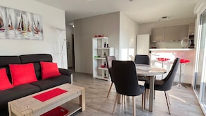 Una sala moderna con un sofá negro, cojines rojos, una mesa de centro de madera y un área de comedor con sillas negras y una mesa blanca.