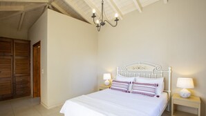 Ein Schlafzimmer mit einem Bett, zwei Nachttischen mit Lampen, einer Kristallleuchtre, einem Holzschrank und einer weißen Decke.