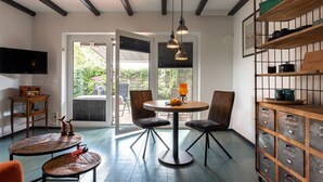 Una habitación con una mesa redonda, dos sillas, un televisor, un mueble de madera y un ventanal con persianas.