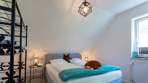 Un dormitorio con cama, mesita de noche, estante en la pared y una ventana.