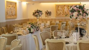Un salón de banquetes con mesas redondas dispuestas para comer, cada una con mantel blanco y un centro de mesa.
