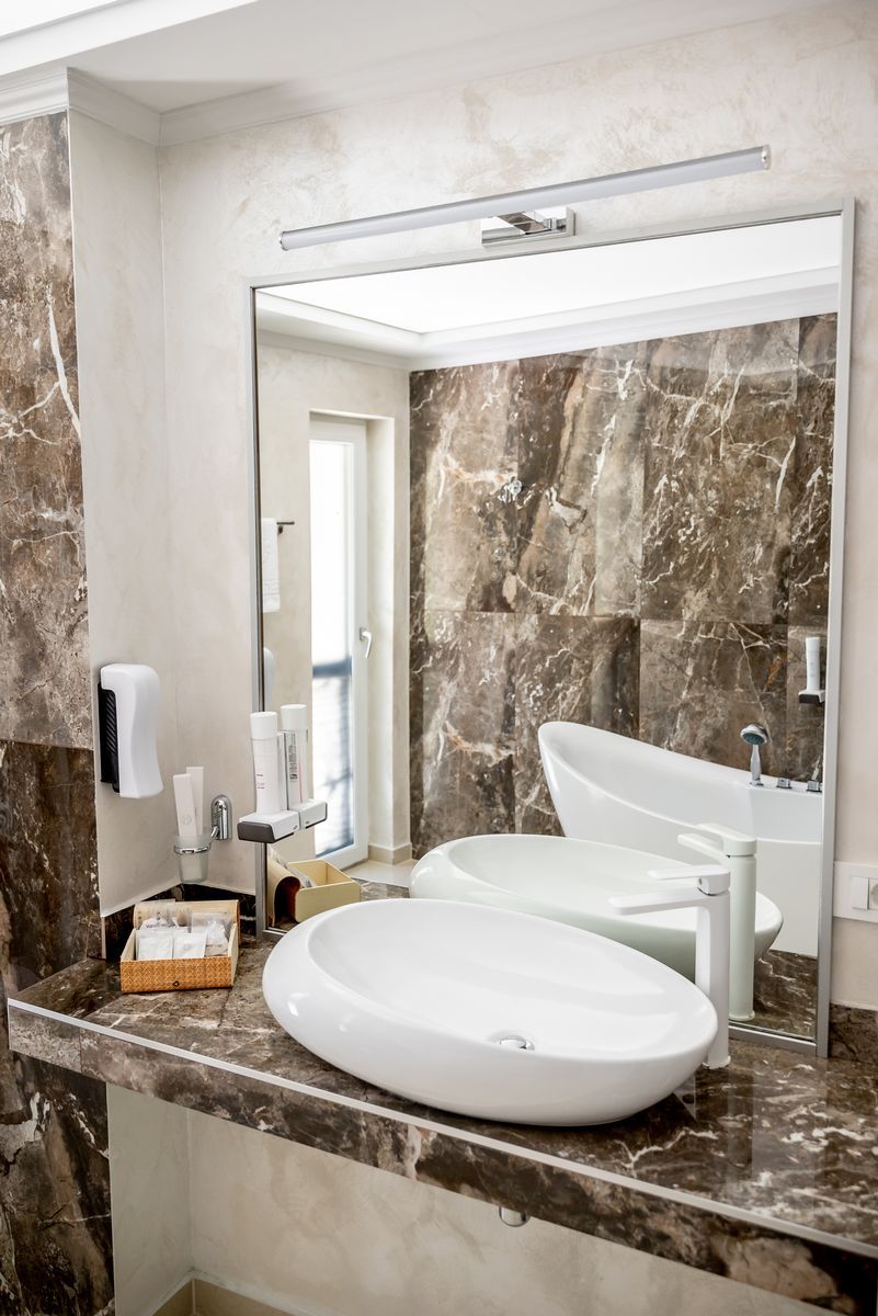 Un baño moderno con pared de mármol, un espejo grande, un lavabo blanco y una bañera independiente.