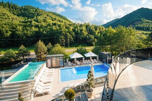 Un área de piscina con sillones de descanso y sombrillas, rodeada de exuberante vegetación y colinas.