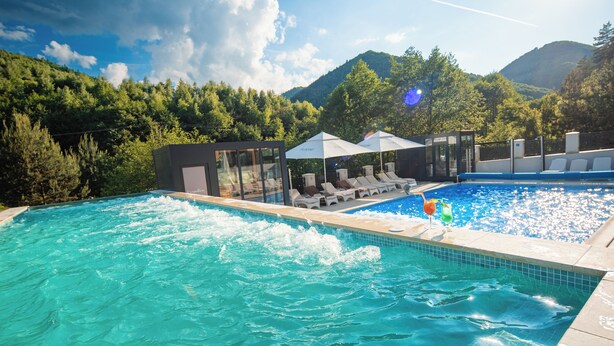Una piscina con sillas de descanso y sombrillas, rodeada de abundante vegetación y montañas.