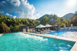 Una piscina con sillas de descanso y sombrillas, rodeada de abundante vegetación y montañas.