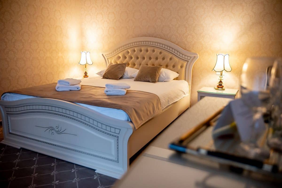 Un lit bien fait, avec une tête de lit capitonnée, deux lampes de chevet et des serviettes pliées posées sur le lit.