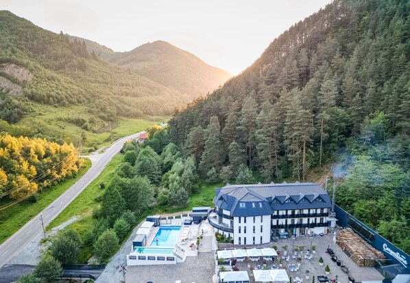 Un hotel con piscina, zona de estar al aire libre y vistas de las colinas boscosas circundantes.