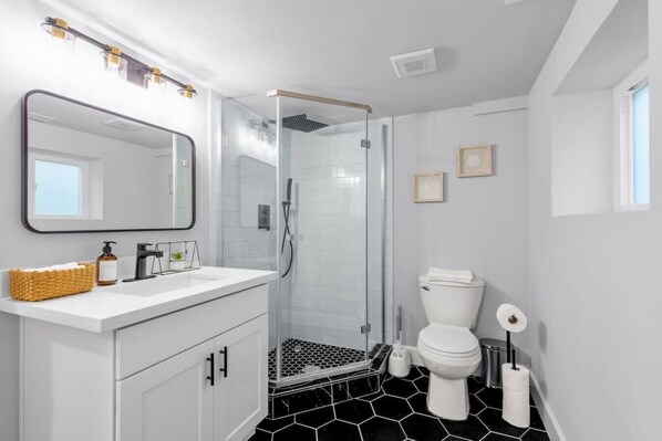 Un baño moderno con ducha de vidrio, un lavamanos blanco con espejo y un inodoro.