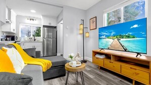 A modern living room with a grey sofa, a wooden TV stand, and a large TV displaying a tropical beach scene.