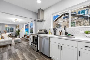 A modern kitchen with white cabinets, stainless steel appliances, and a large window offering a view of the outside.