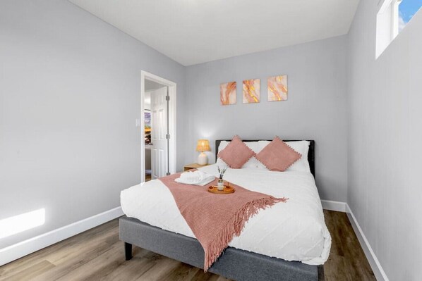 A bedroom with a bed, a bedside table, a lamp, and a door leading to another room.