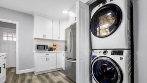 Una cocina moderna con armarios blancos, un refrigerador de acero inoxidable, un microondas y una lavadora y secadora apiladas.