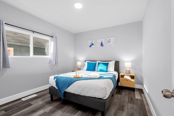 A modern bedroom with a bed, bedside tables, a window with curtains, and artwork on the wall.