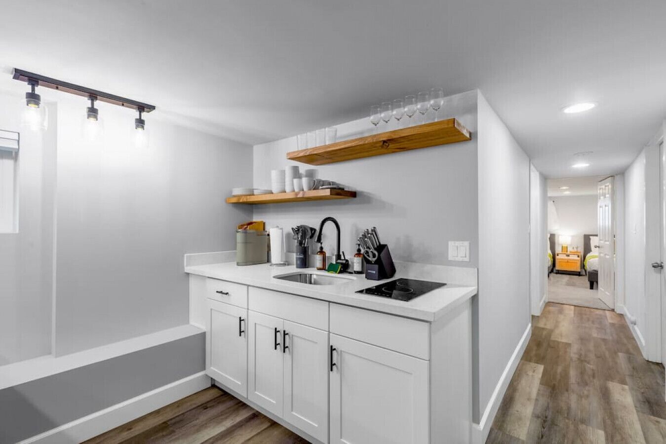 A modern kitchen with white cabinetry, a black stove, and a wooden shelf above the sink.