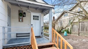 Une maison avec un porche en bois à l’avant, une porte blanche et un petit jardin.